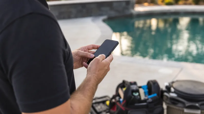 Pool technician holding a smartphone poolside while recording a service checklist